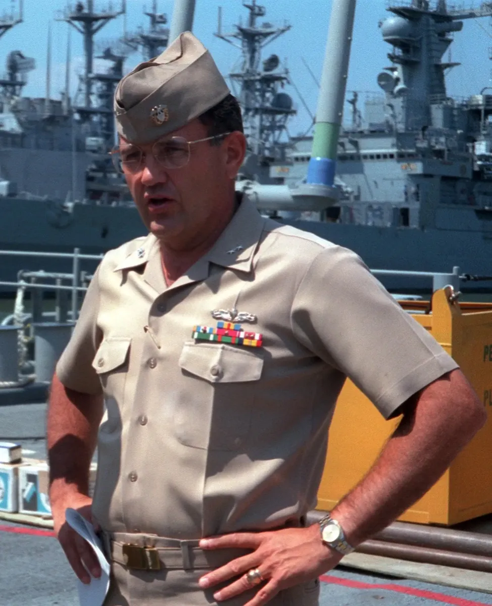 Rear Admiral Philip A. Dur in khaki service uniform on the pier, warships moored behind him